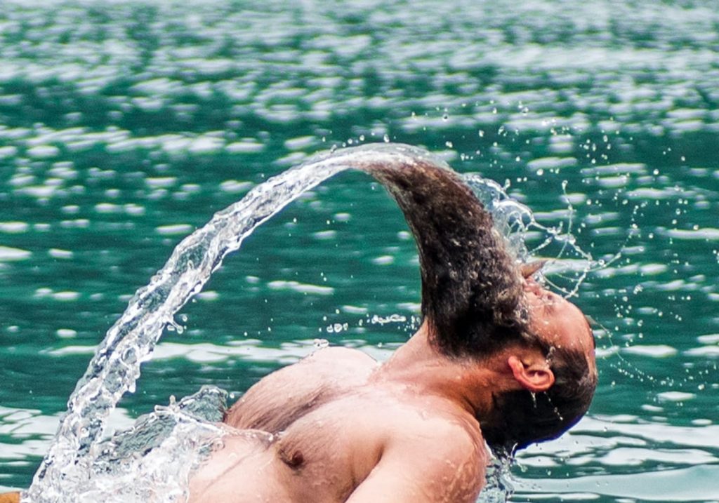 Homme barbu dans l'eau qui se jette en arrière formant un arc d'eau