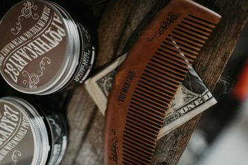 Peigne barbe posé sur un billet américain le tout sur une table avec des baumes à barbe